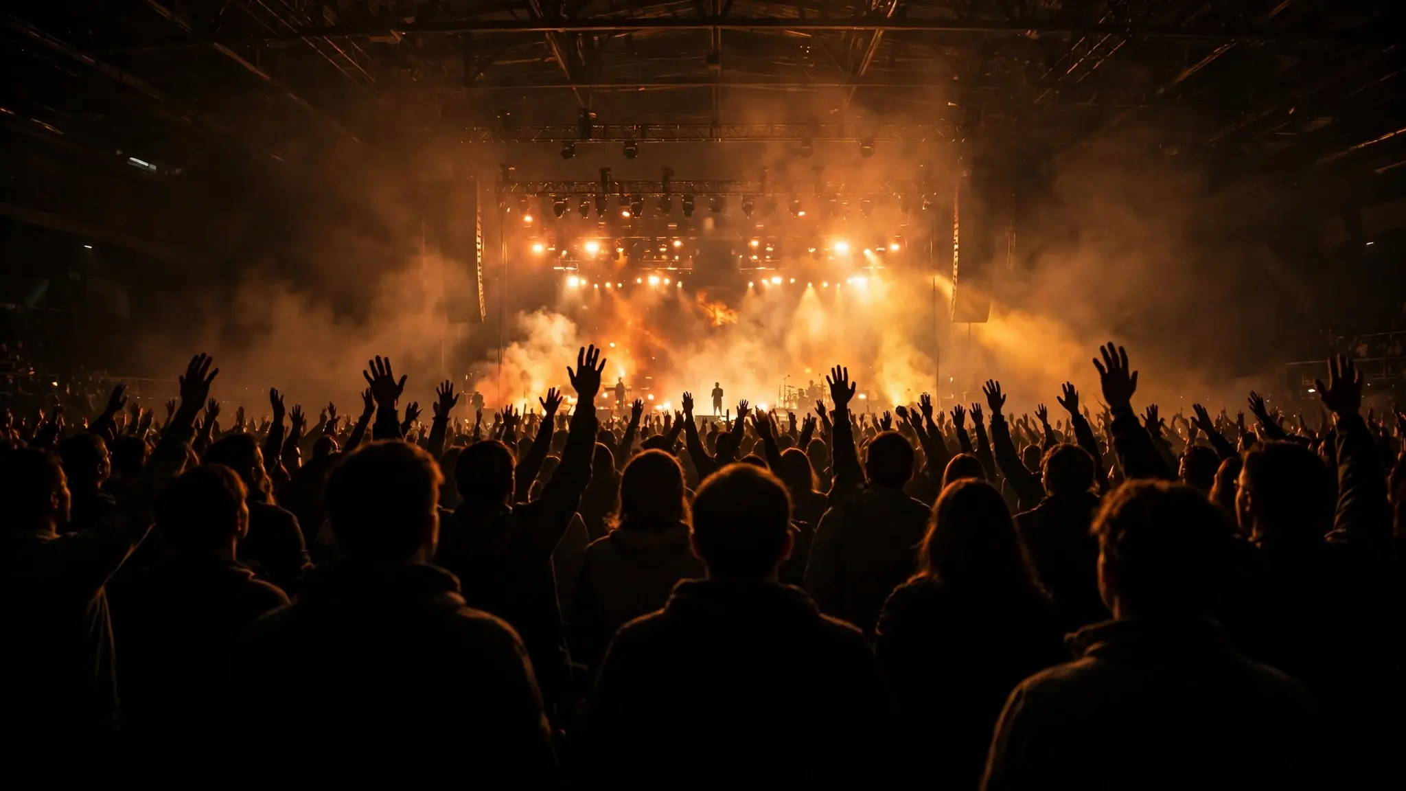 A concert crowd with raised hands under bright stage lights, seen from behind the audience at a large worship music show