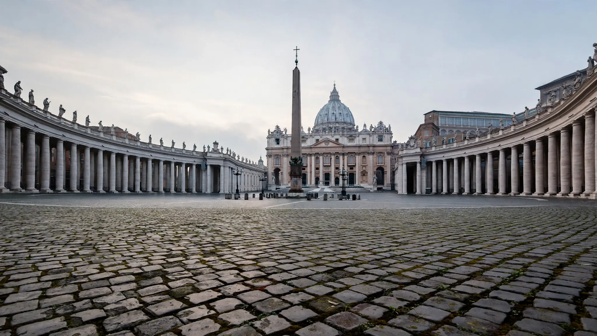 A wide view of St. Peter's Basilica colonnade in Rome under a pale morning sky with empty cobblestones in the foreground